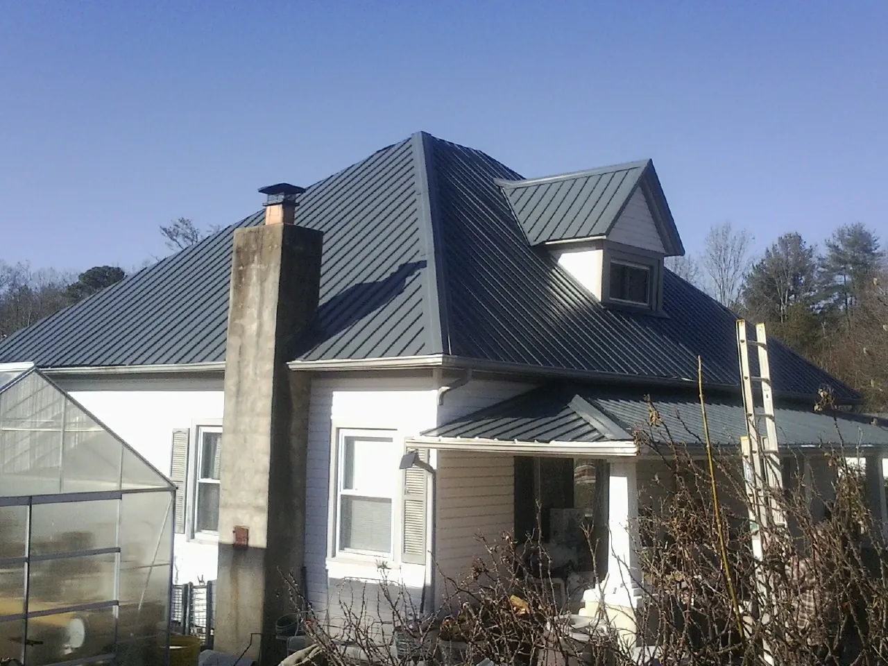Dark blue standing seam metal roof on a white farmhouse with dormer — Slate & Tile Roof Repair by Roofing Brothers in Northwood
