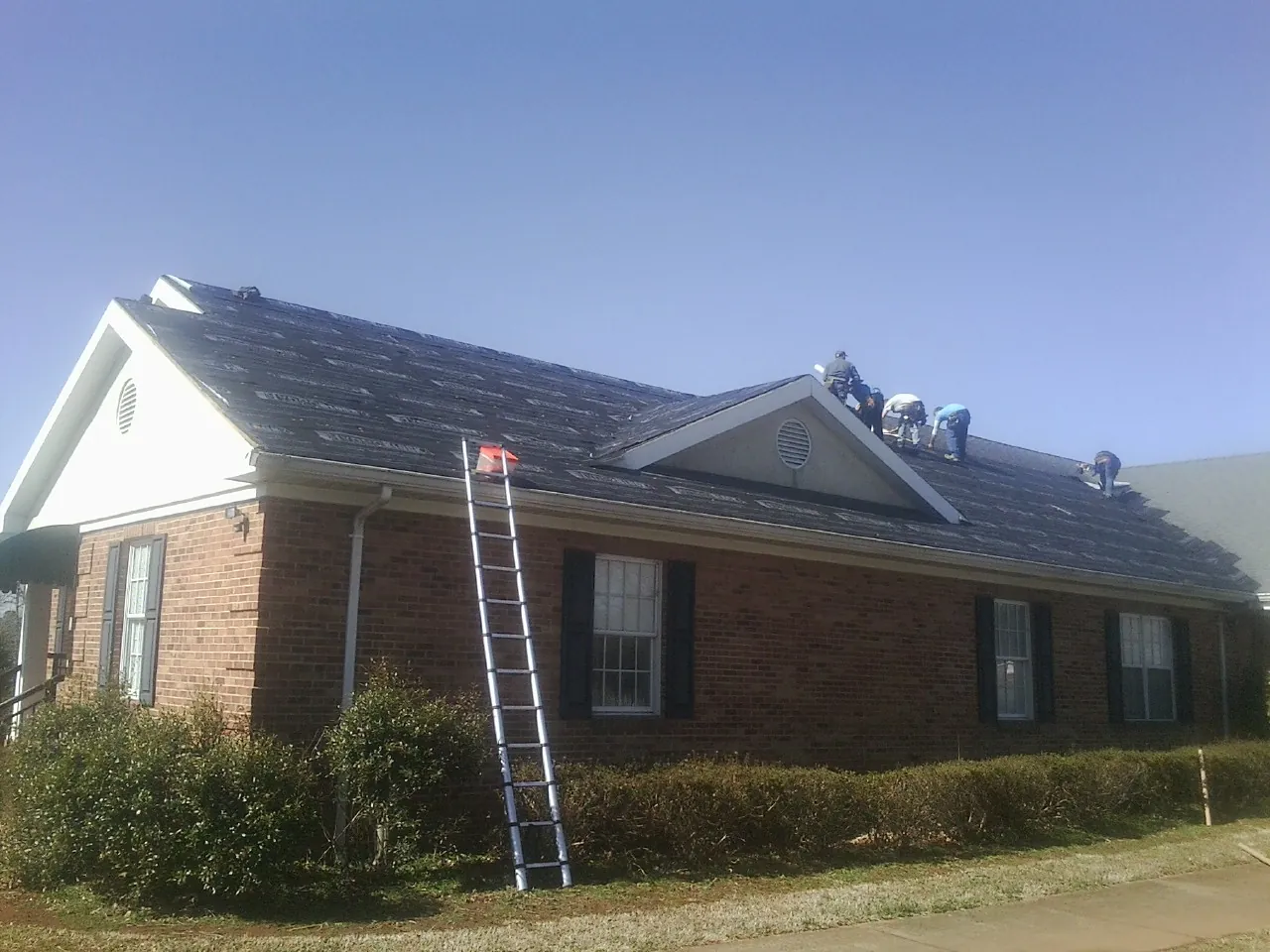 Crew tearing shingles off a brick ranch roof with a ladder set — Metal Roof Repair work by our crew in Northwood