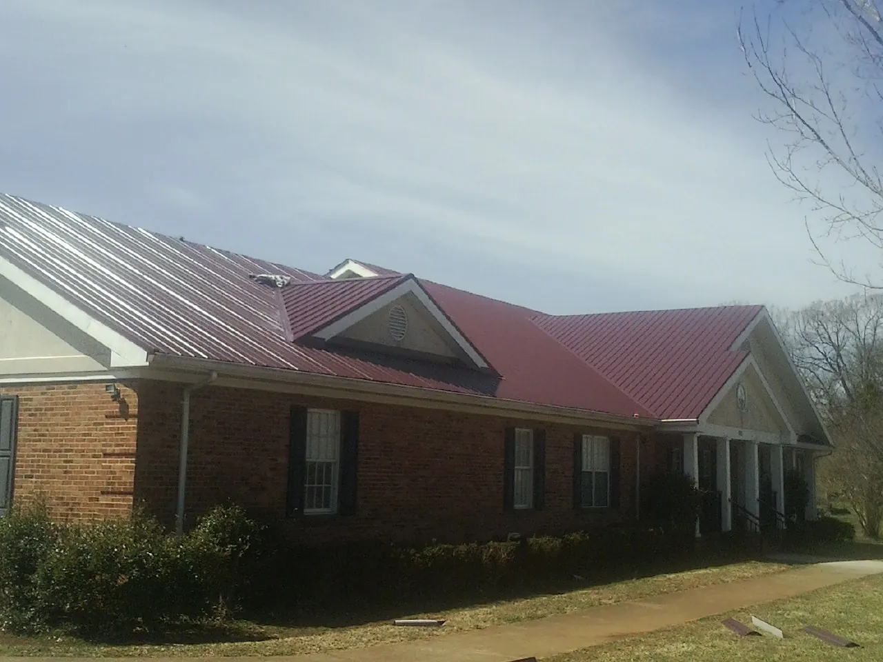 Red metal roof with gabled entries on a long brick building, from a Hail Damage Roof Repair job in Northwood