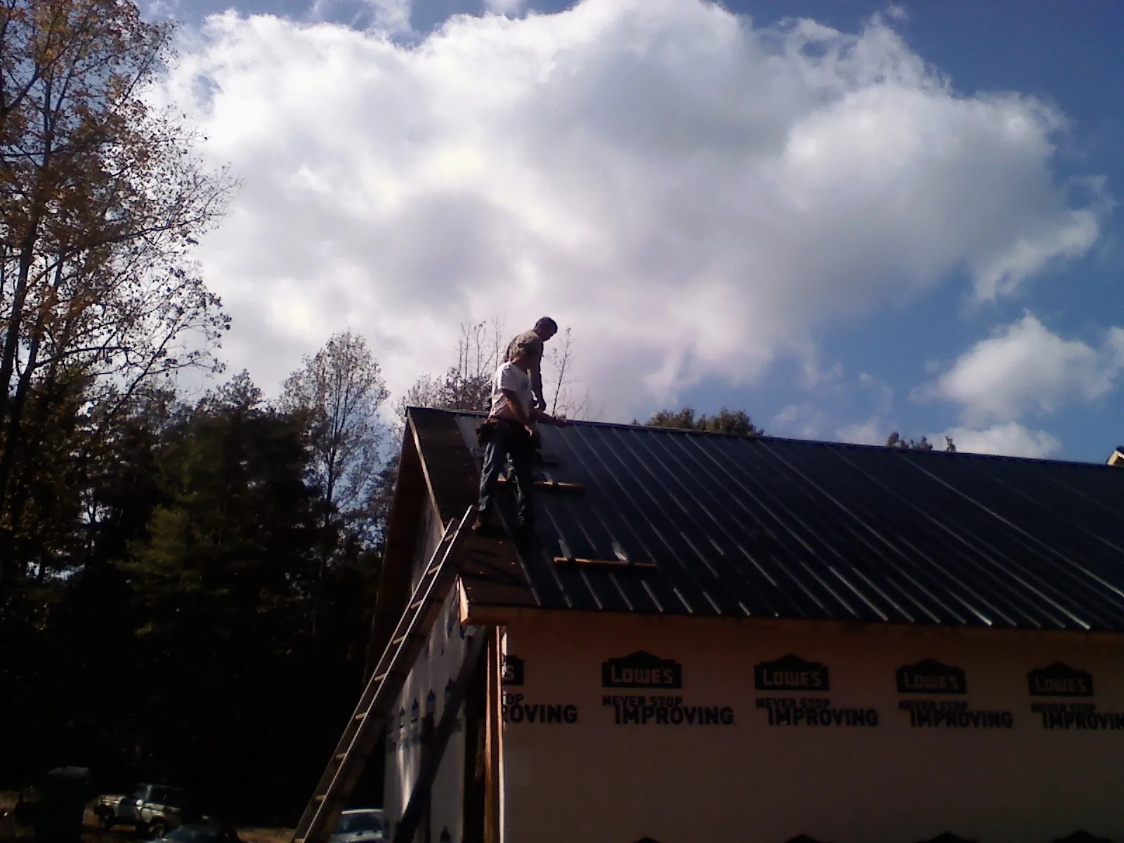 Roofer fastening dark metal panels high against a cloudy sky, from a Roof Inspection job in Northwood