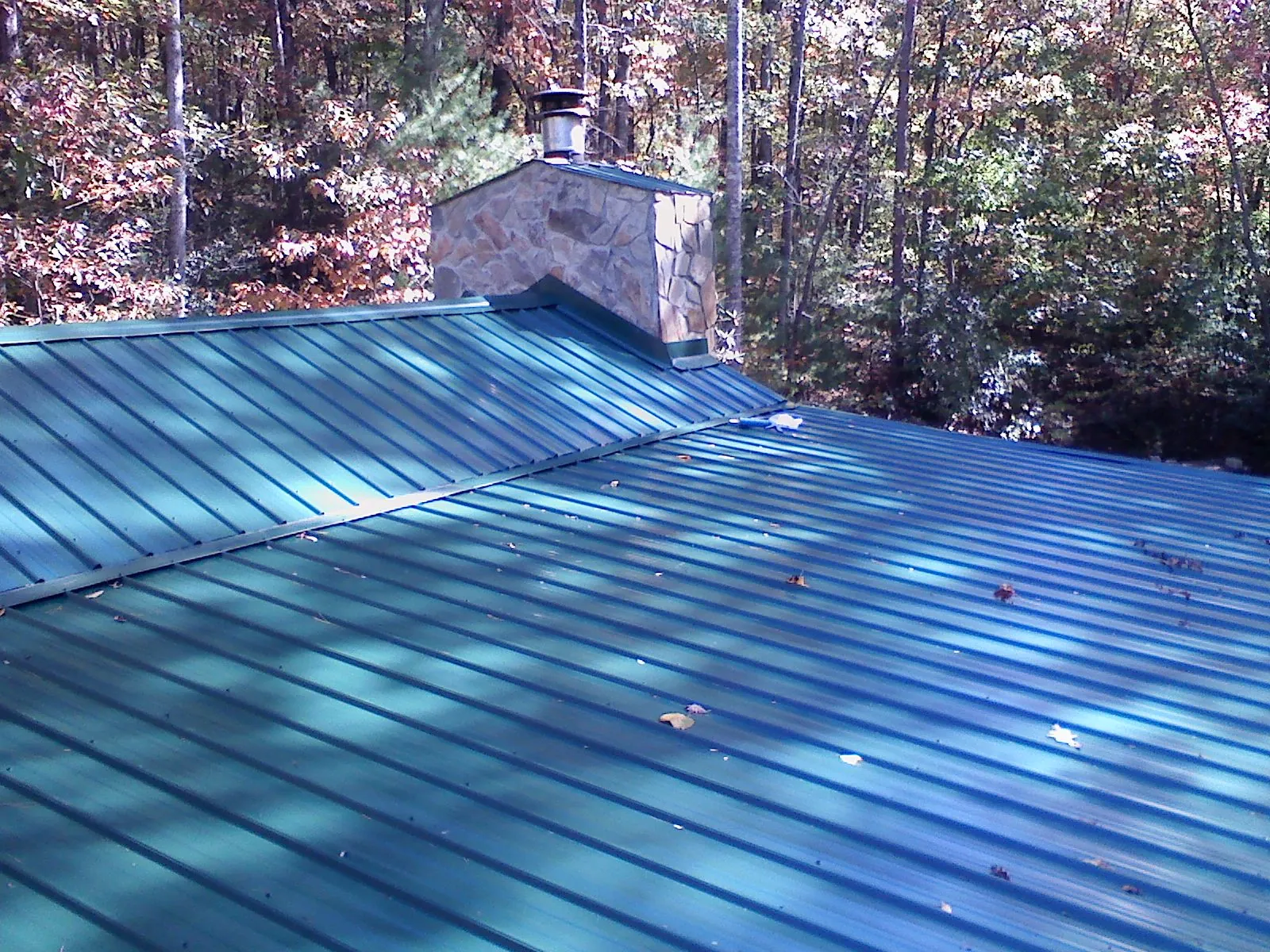 New green metal roof and stone chimney surrounded by autumn woods in Northwood