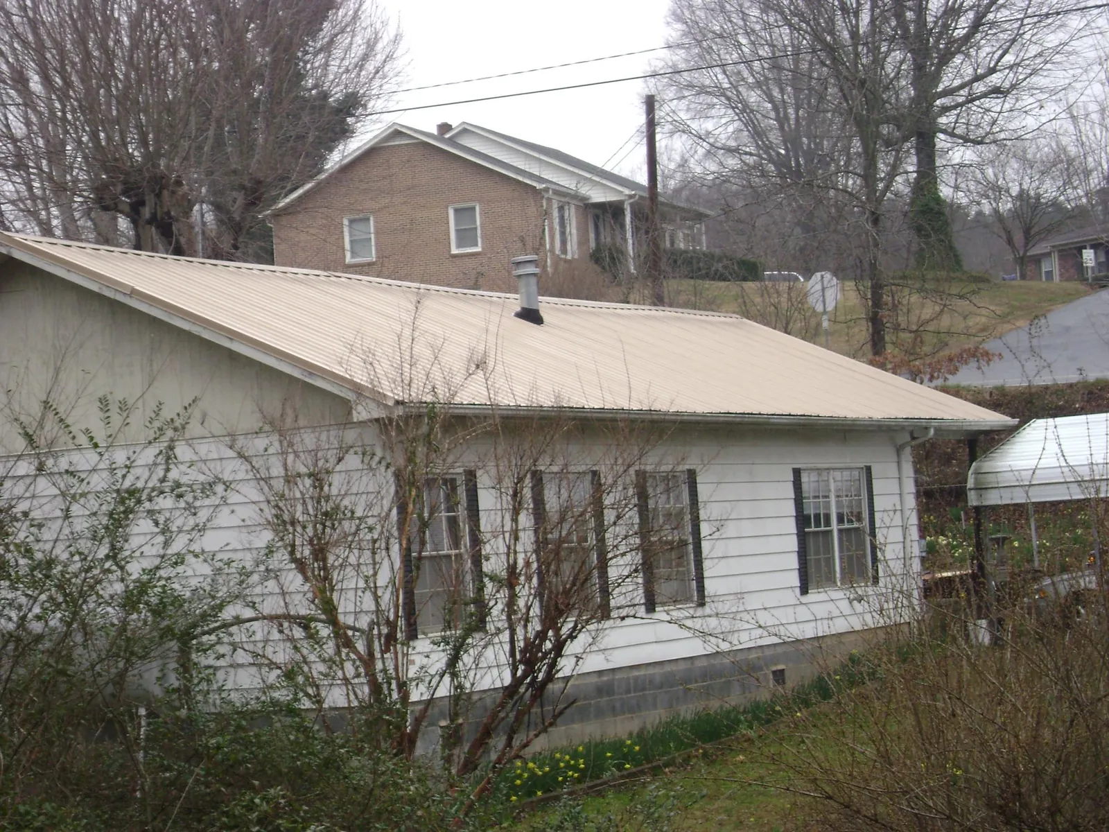 Tan metal roof on a white sided house set into a hillside — Commercial Roofing by Roofing Brothers in Northwood